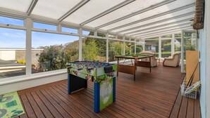 Un espacio interior iluminado por el sol, con mesa de fútbol, mesa de billar y asientos cómodos.
