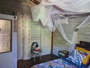 A room with a bed, a chair, a small table, and a mosquito net. - Bungalow (Sainte-Anne)
