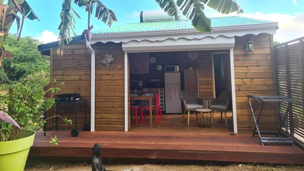 Ein Holzhaus mit überdachter Terrasse, einer kleinen Küchenzeile und einer Sitzecke mit Stühlen und Tisch.
