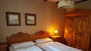 Een tweepersoonsbed met witte lakens, twee nachtkastjes, een nachtkastje met lamp en een houten garderobe met bloemversieringen.