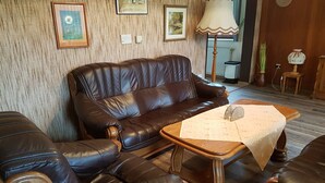 Een woonkamer met een bruine leren bank, een houten salontafel en bijpassende fauteuils.