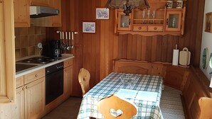 Een kleine keuken met houten kastjes, een eettafel met geruit tafelkleed en een houten bank.