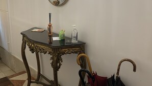 A hallway with a decorative mirror, a table with a bottle and a teapot, and a vintage umbrella stand. - Three bedroom apartment in Venice San Marco (Venezia)