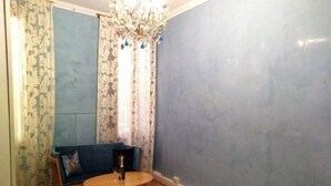 A room with a blue wall, a wooden floor, a round table with a chair, a sofa with a cushion, and a chandelier. - Three bedroom apartment in Venice San Marco (Venezia)