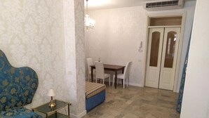 A room with a blue sofa, a small table with a lamp, a bench, a dining table with chairs, and a wardrobe. - Three bedroom apartment in Venice San Marco (Venezia)