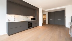 A modern kitchen with grey cabinets, a built-in oven, and a marble backsplash.