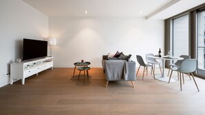 A modern living room with a flat-screen TV, a sofa, a coffee table, and a dining area with chairs and a table.
