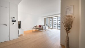 A spacious living area with a sofa, coffee table, and a large window offering a view of buildings.