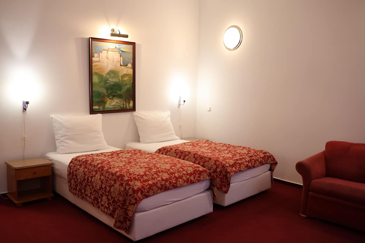 Una habitación de hotel con dos camas, un sofá rojo, un cuadro en la pared y una lámpara de pared redonda.