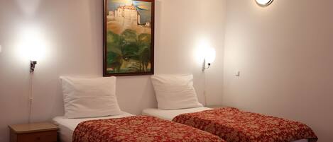 A hotel room with two beds, each with a red floral bedspread, white pillows, and a painting of a castle on the wall.