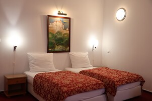 Een hotelkamer met twee bedden, elk voorzien van een rood bloemenbedekking, witte kussens, en een schilderij van een kasteel aan de muur.