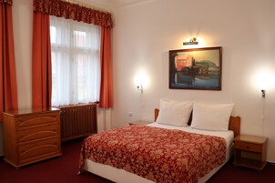 Habitación de hotel con cama, cómoda de madera, radiador y un cuadro en la pared.