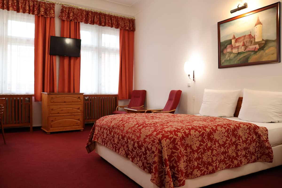 Una habitación de hotel con una cama, un aparador de madera, un televisor y un cuadro de un castillo en la pared.