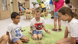 Des enfants participaient à une activité avec des bâtons sur un tapis vert, dans une salle de classe.