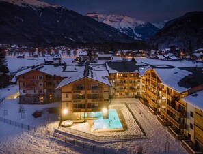Estância coberta de neve com vários edifícios, uma piscina central e montanhas ao fundo.
