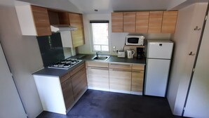 A compact kitchen with a gas stove, sink, microwave, and a small refrigerator. - Mobil home 6 pers camping 3* sur belle parcelle au calme avec piscine (Saint-Chéron)