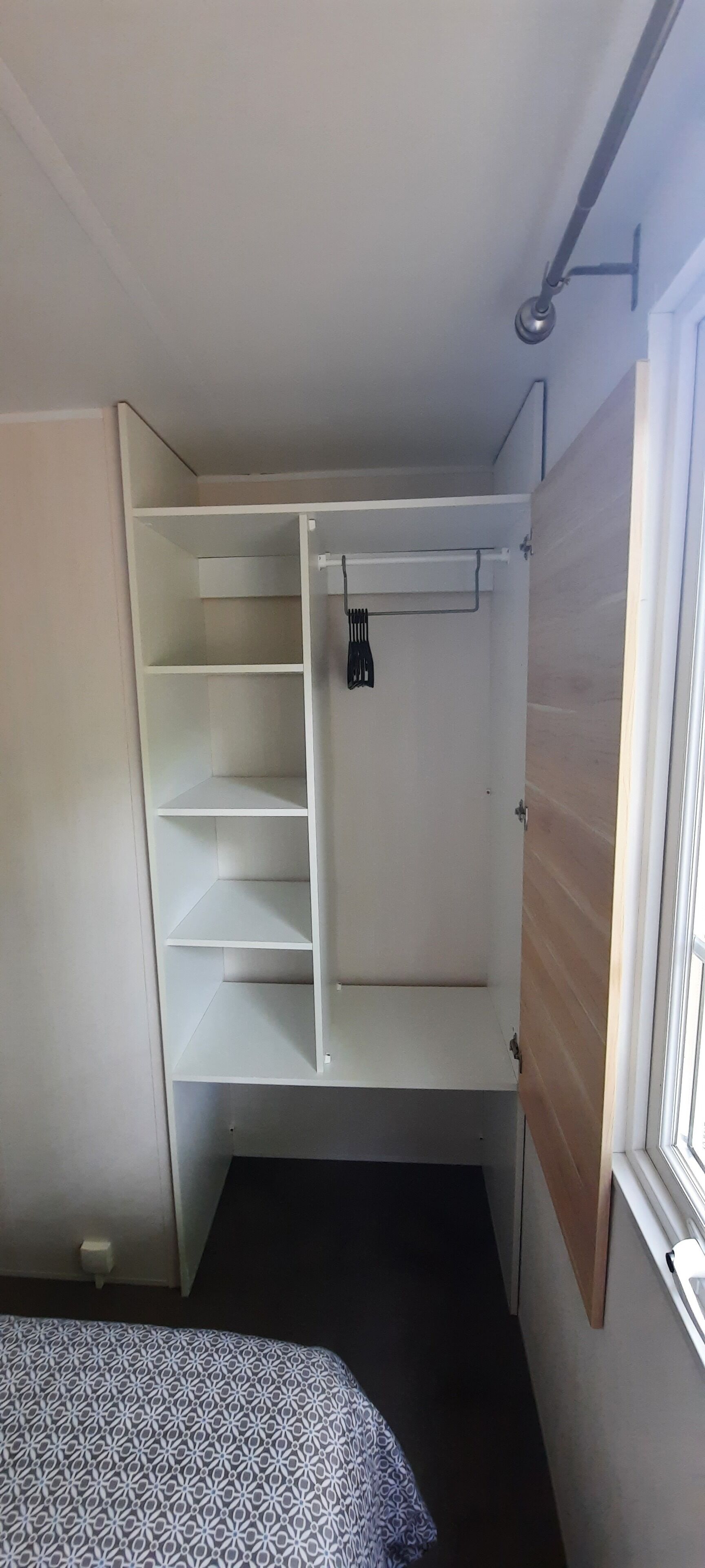 Een hoek slaapkamer met een inbouwkast, een bed met beddengoed met een patroon, en een raam.