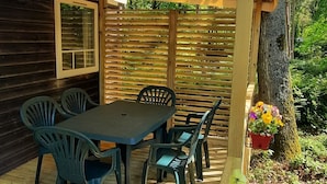 A wooden deck with a covered outdoor seating area, a table with chairs, and potted flowers. - Mobil home 6 pers camping 3* sur belle parcelle au calme avec piscine (Saint-Chéron)