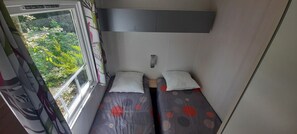 A small, narrow room with two beds, a window with curtains, and a view of greenery outside. - Mobile home for 6 people, 3-star campground on a beautiful, quiet property with a pool (Saint-Chéron)