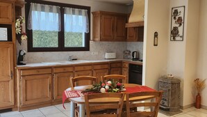 Une cuisine avec des meubles de rangement en bois, une table à manger avec des chaises, une fenêtre avec des rideaux et un élément décoratif en métal accroché au mur.