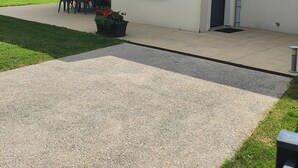 Une maison moderne dotée d’un patio, d’un coin repas avec des chaises et d’un petit jardin.
