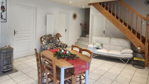 Un coin repas avec une table en bois, des chaises et une décoration de table festive. Un escalier avec des rampes en bois mène à un salon doté d’un canapé blanc et d’une petite table d’appoint.