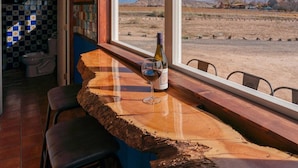 Um balcão de madeira rústico com uma garrafa de vinho e um copo, com vista para uma paisagem desértica.