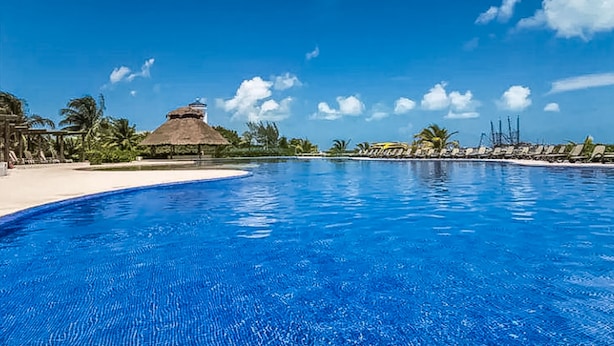 A clear blue pool with a thatched-roof structure and lounge chairs along the edge. - AMARA Beachfront Apartments by The Sea (Villa de Cos)