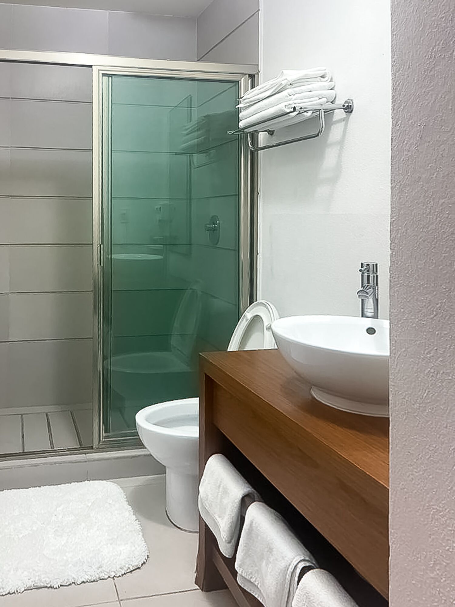 A bathroom with a glass shower enclosure, a white toilet, and a wooden vanity with a sink.