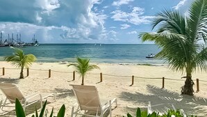 A beach with white lounge chairs, a palm tree, and a view of the ocean with boats in the distance. - AMARA Beachfront Apartments by The Sea (Villa de Cos)