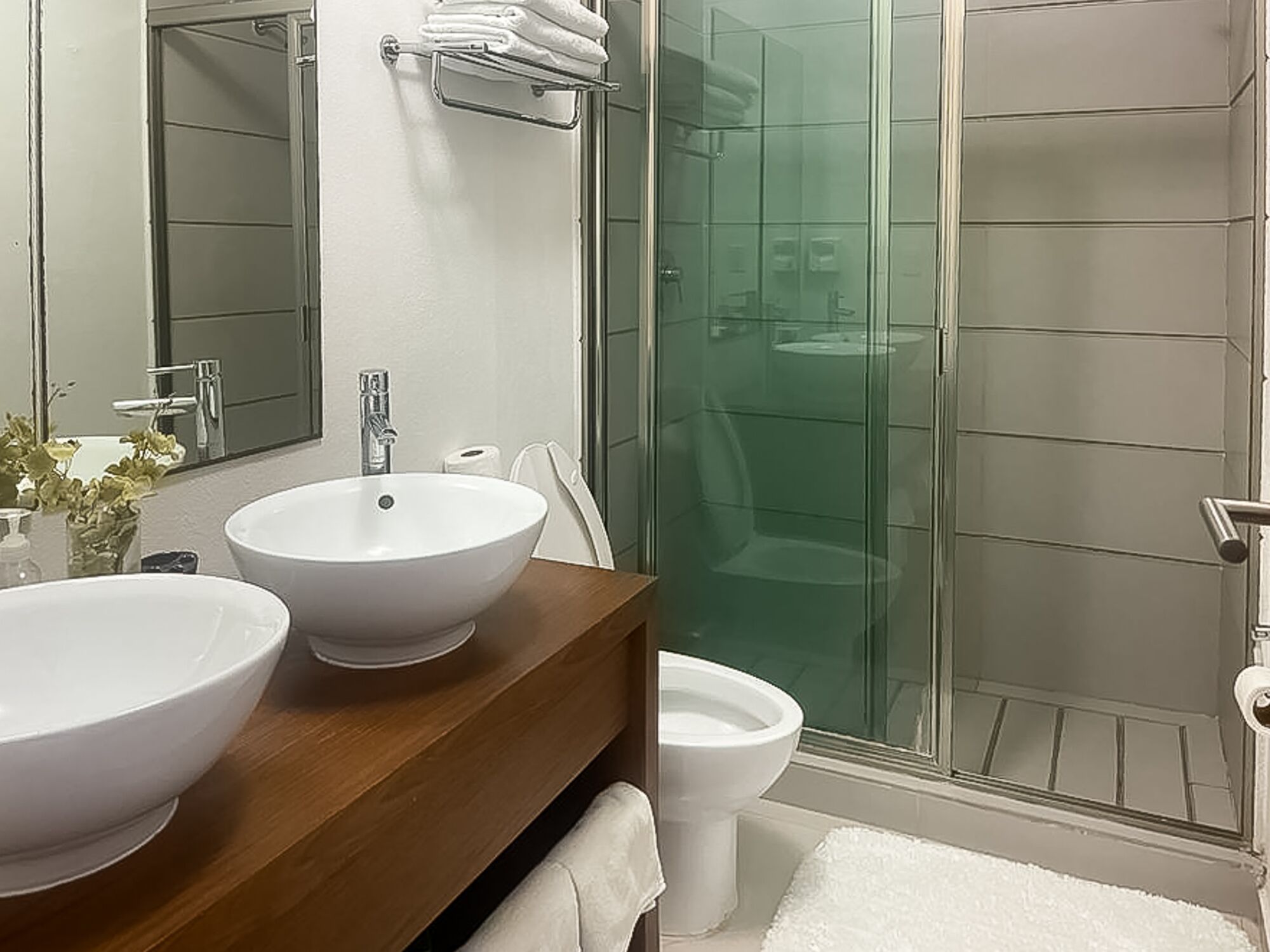 A bathroom with a large white sink, a mirror, a glass shower enclosure, and a toilet.