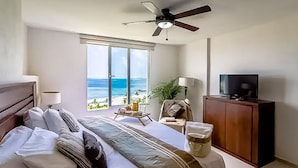 A hotel room with a bed, a television, a ceiling fan, a plant, and a view of the ocean. - AMARA Beachfront Apartments by The Sea (Villa de Cos)