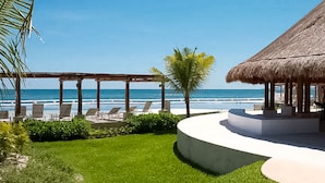 A beachside resort with a thatched-roof structure, lounge chairs, and a view of the ocean. - AMARA Beachfront Apartments by The Sea (Villa de Cos)