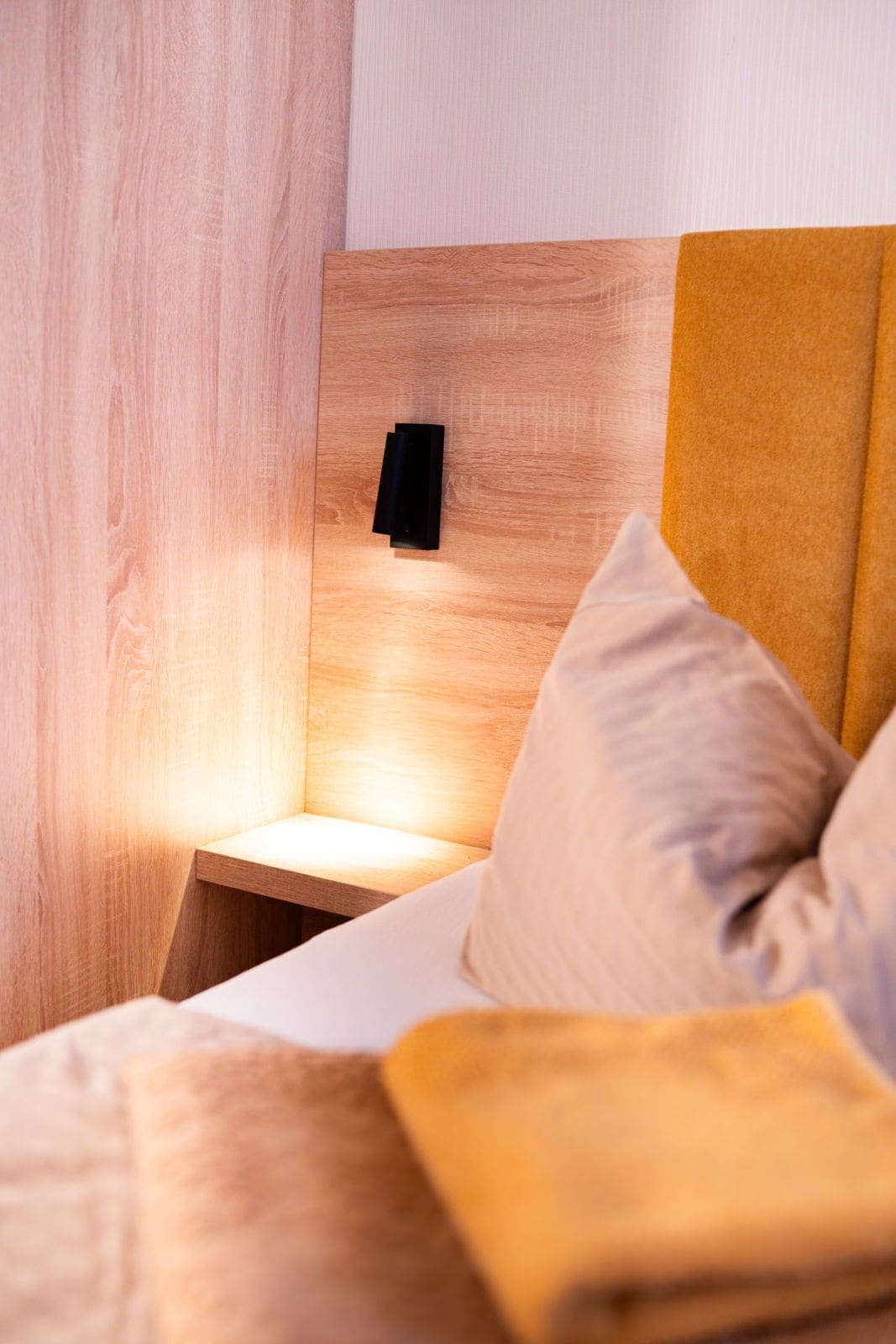 A modern bedroom with a wooden headboard, a bedside table, and a bed with a yellow blanket.