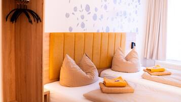 Quarto de hotel com guarda-roupa de madeira, cabeceira com padrão floral e cama com almofadas bege e toalha dobrada.