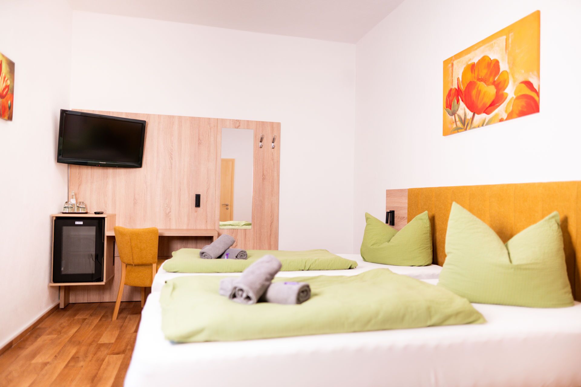 Habitació d'hotel amb dos llits, una televisió, nevera petita i armari de fusta.