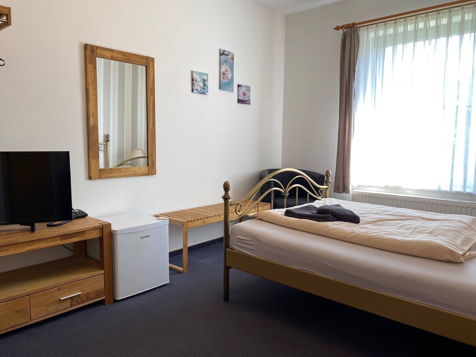A bedroom with a bed, a desk with a chair, a television, and a small refrigerator.