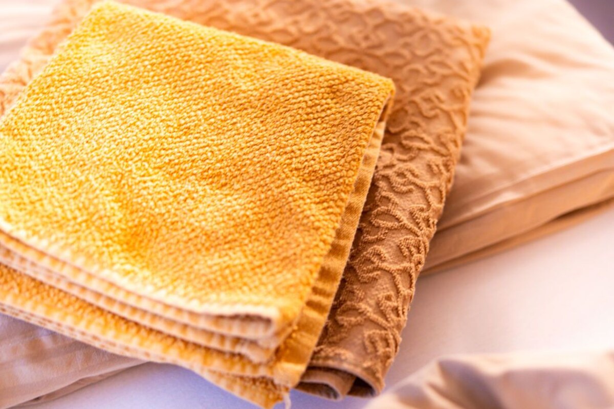Un lit avec du linge de lit beige et une serviette jaune pliée.