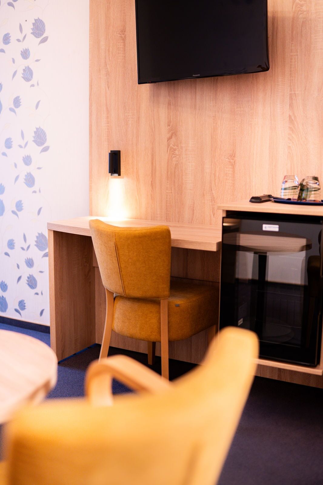 Una habitación moderna con un escritorio de madera, una silla amarilla, un televisor de pantalla plana montado en la pared y un horno o microondas pequeño.