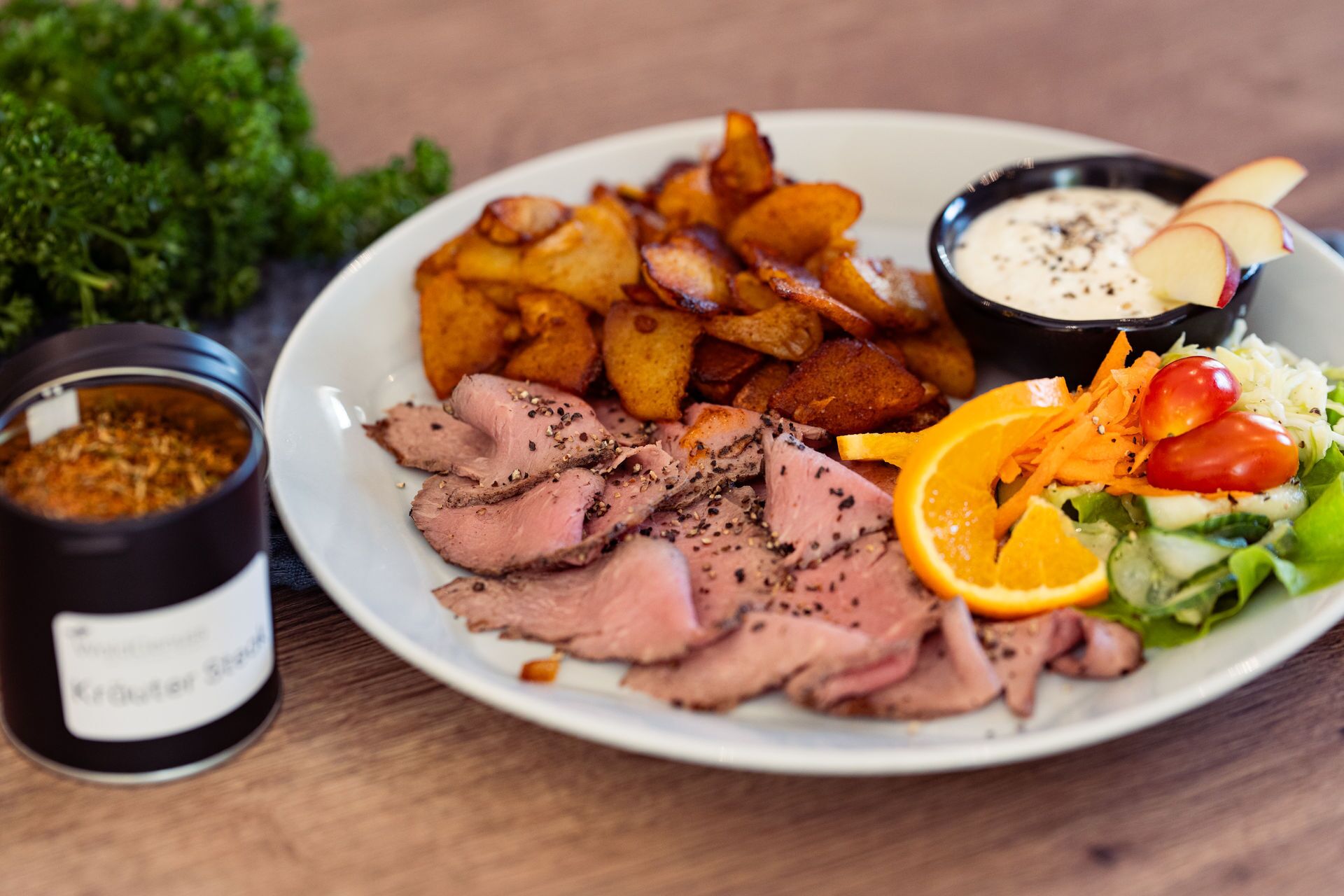 A plate with sliced meat, roasted potatoes, a salad, and two dipping sauces.