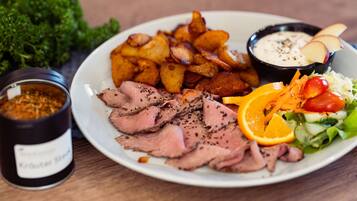 A plate with sliced meat, roasted potatoes, a salad, and two dipping sauces.