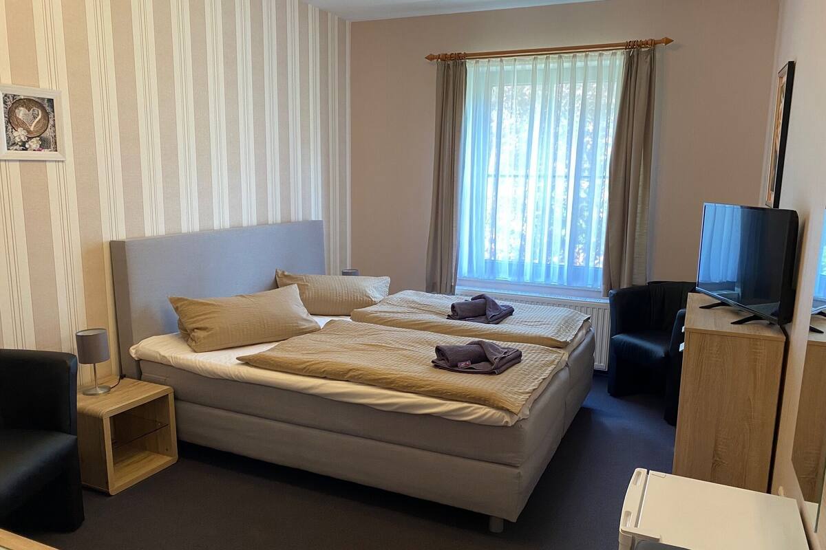 Une chambre d’hôtel avec un grand lit, un bureau, une chaise, une télévision et une fenêtre avec des rideaux.