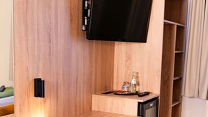 Een kleine kamer met een houten bureau, een enkele gele stoel, een wandgemonteerde televisie en een ingebouwde minibar.