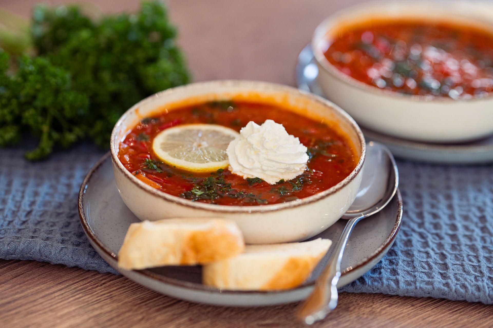 Two bowls of soup with lemon slices and dollops of cream, accompanied by a piece of bread on a textured cloth.