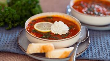 Two bowls of soup with lemon slices and dollops of cream, accompanied by a piece of bread on a textured cloth.