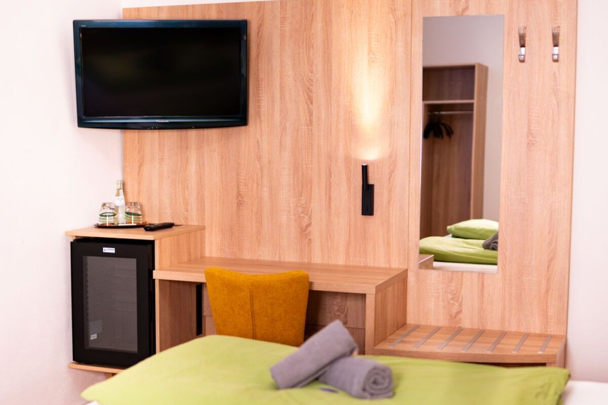 Ein Hotelzimmer mit Bett, Wandfernseher, kleinem Schreibtisch und Kleiderschrank.