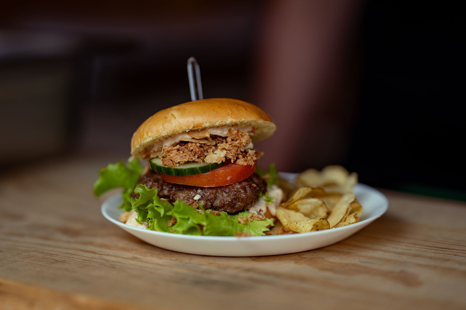 Una hamburguesa con pan, lechuga, tomate y algo frito, servida con papas fritas en un plato blanco.