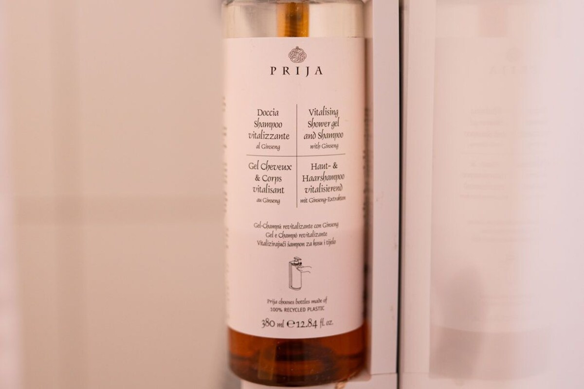 A bottle of PRIJA shampoo and shower gel attached to a wall in a bathroom.