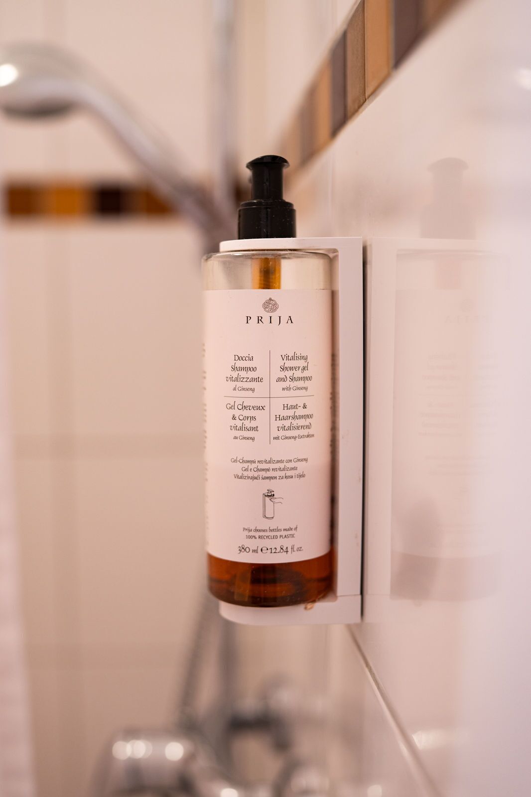 A bottle of PRIJA shampoo and shower gel attached to a wall in a bathroom.