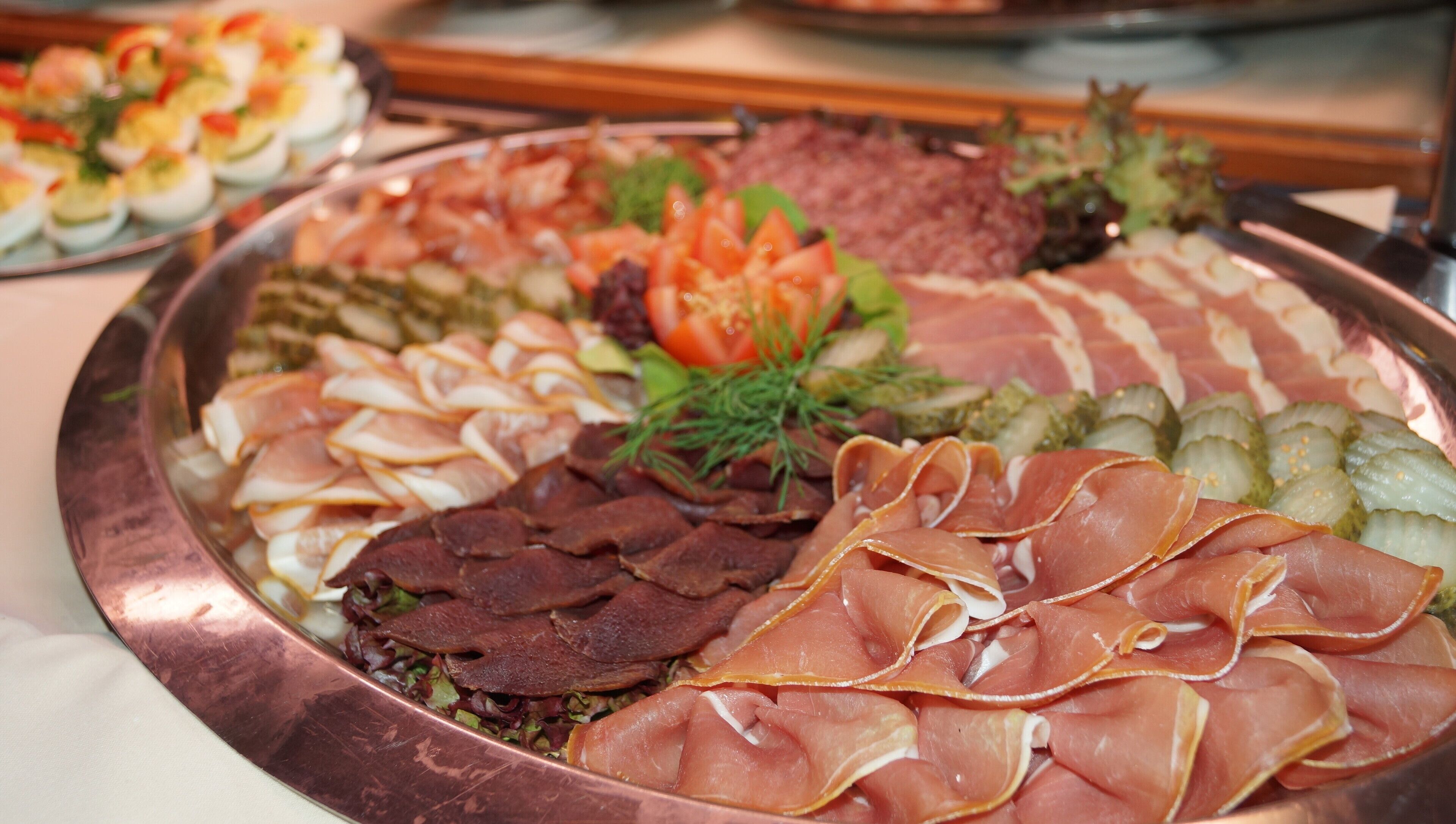 A platter of various meats and cheeses, including prosciutto, salami, and sliced ham, arranged on a copper platter.